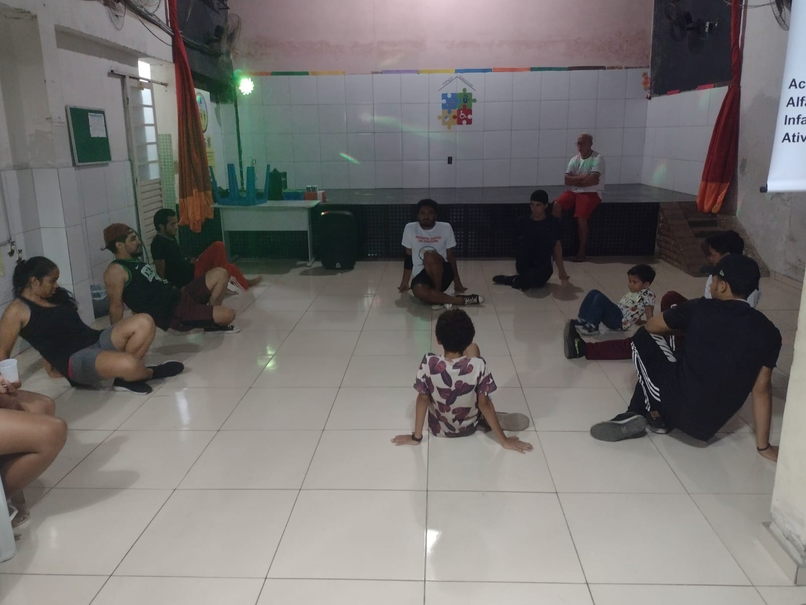 Grupo sentado em círculo no chão do salão da Fundação, no encontro do projeto de ciranda.